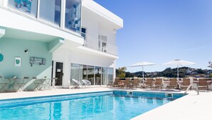 A modern pool area with lounge chairs and umbrellas, a clear blue sky, and a view of a hillside. - Boutique Hotel Casa do Outeiro - Arts & Crafts (Batalha)