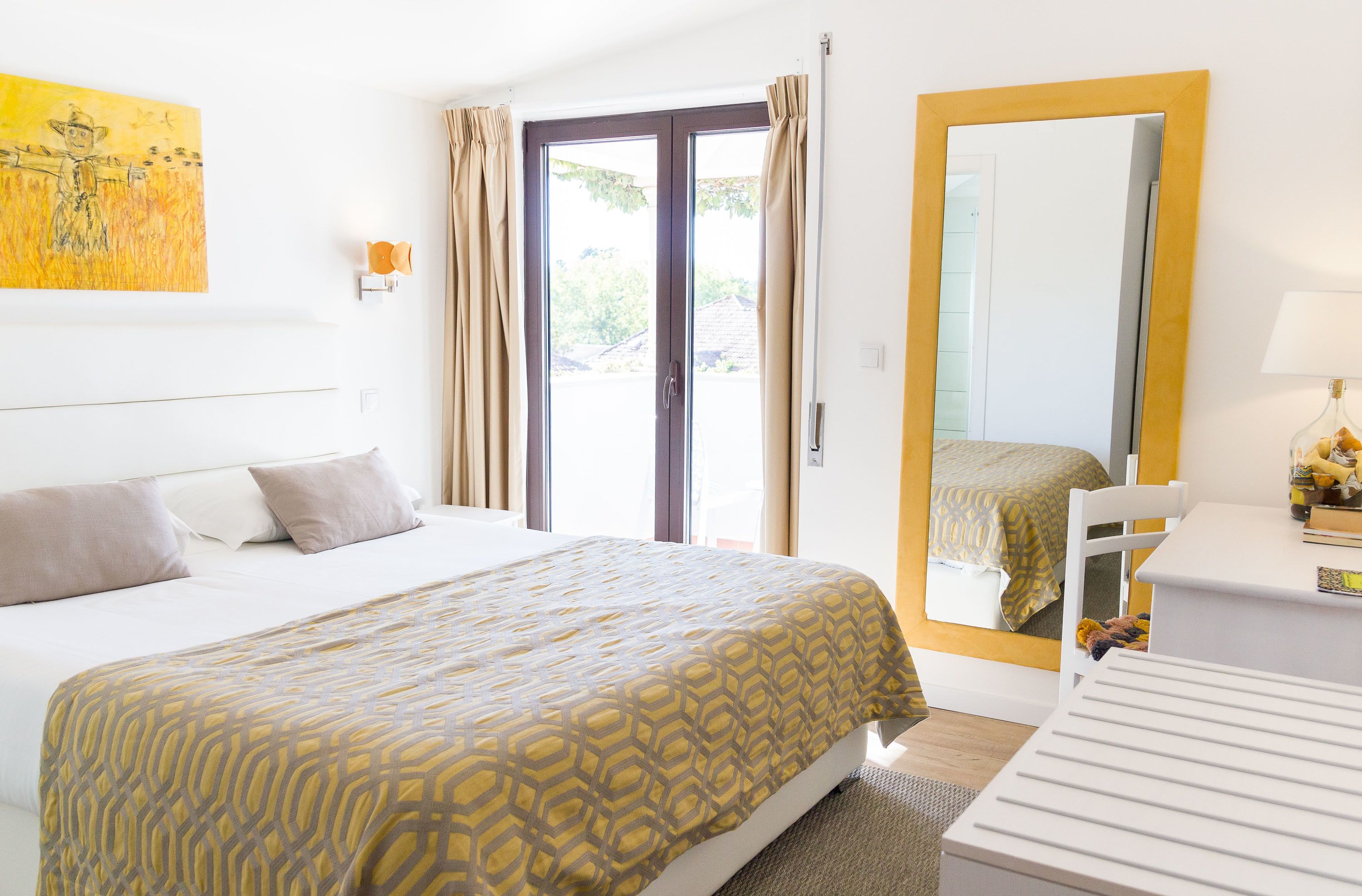 A hotel room with a bed, a desk, a chair, a window with curtains, and a door.