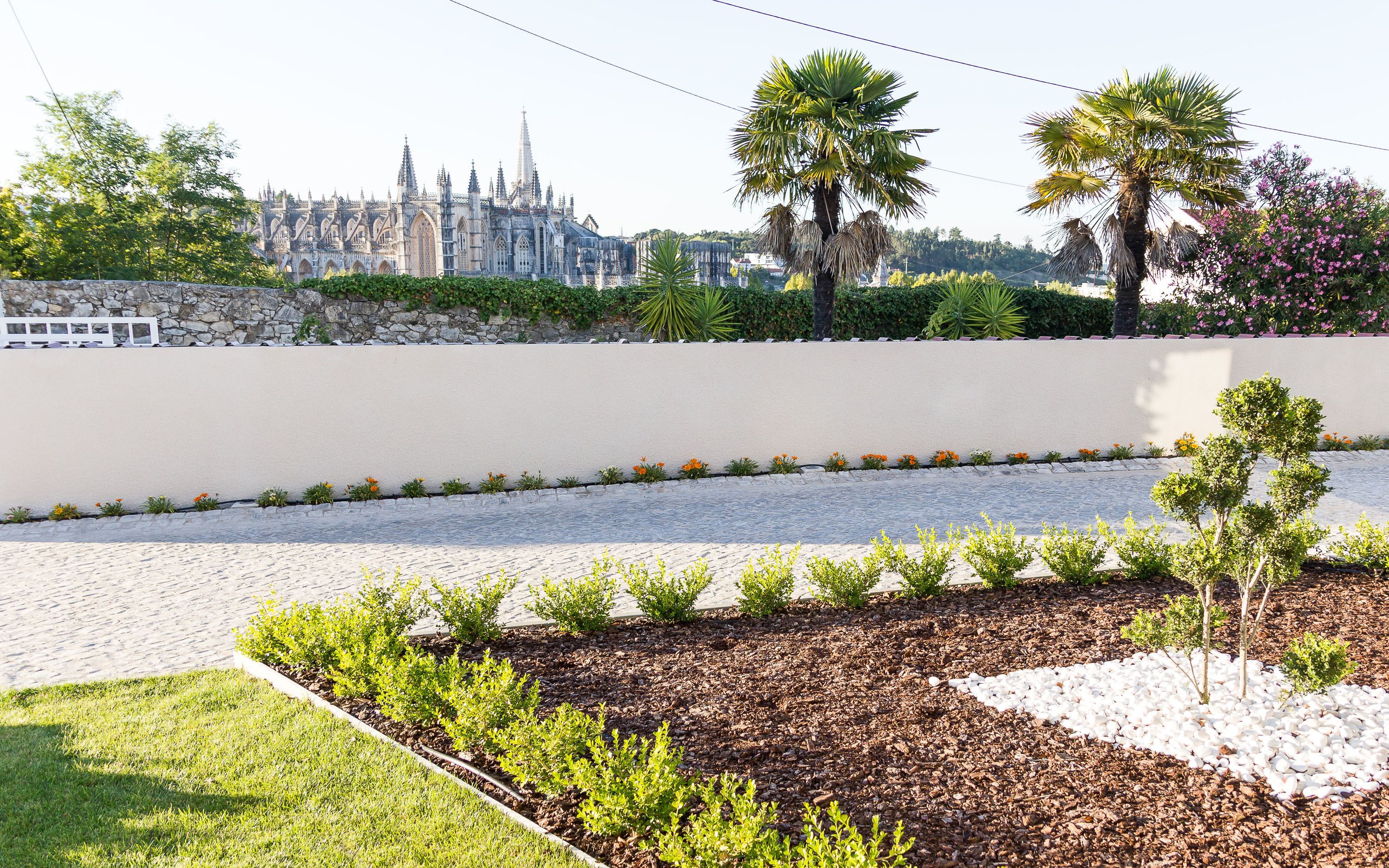 Um jardim ajardinado com um caminho pavimentado, sebes aparadas e diversas plantas.