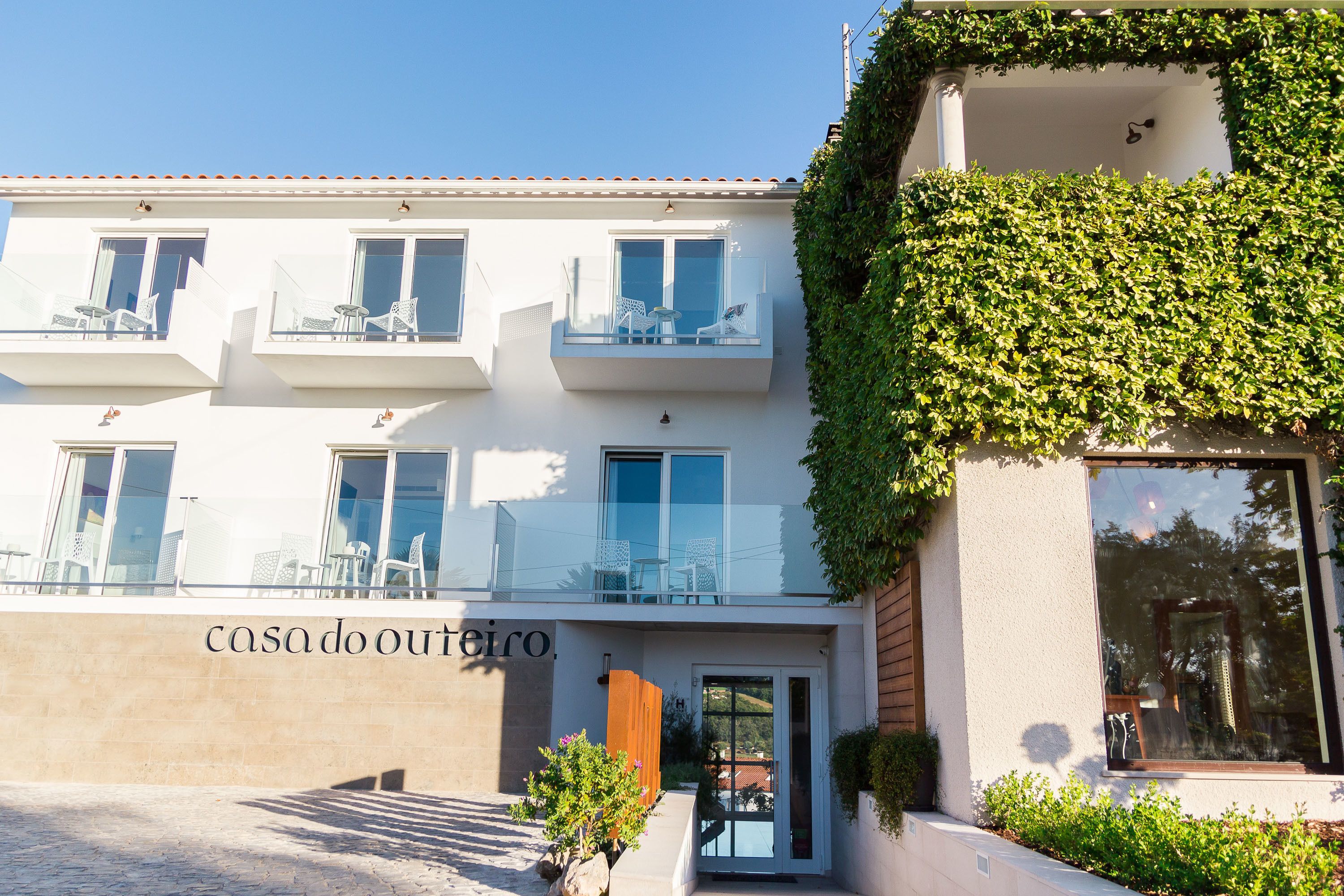 A modern building with a white facade, balconies with outdoor seating, and a sign reading "casado outiro."