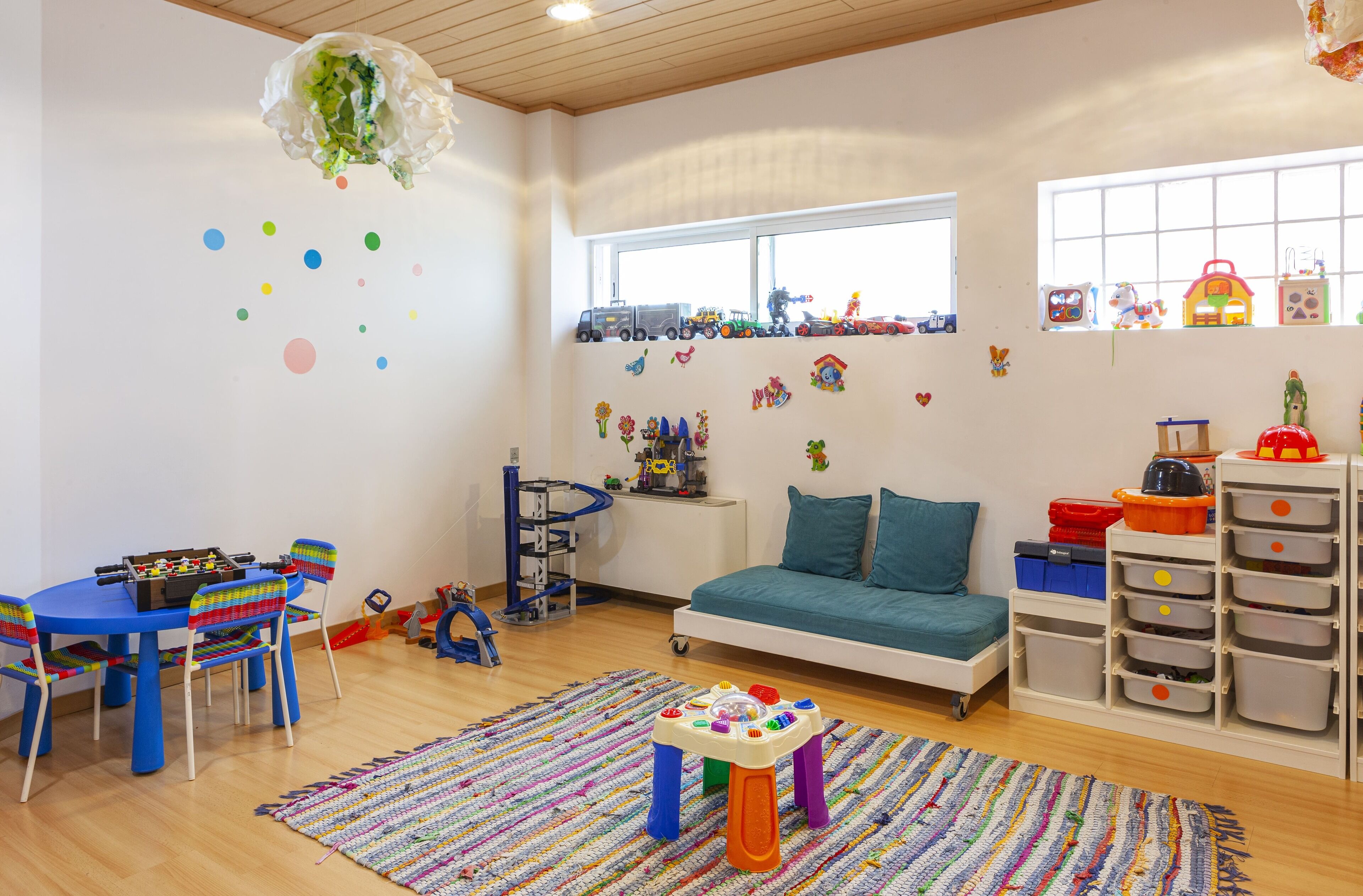 A child-friendly room with a play table, a sofa, a toy storage unit, and a window with toys on the sill.