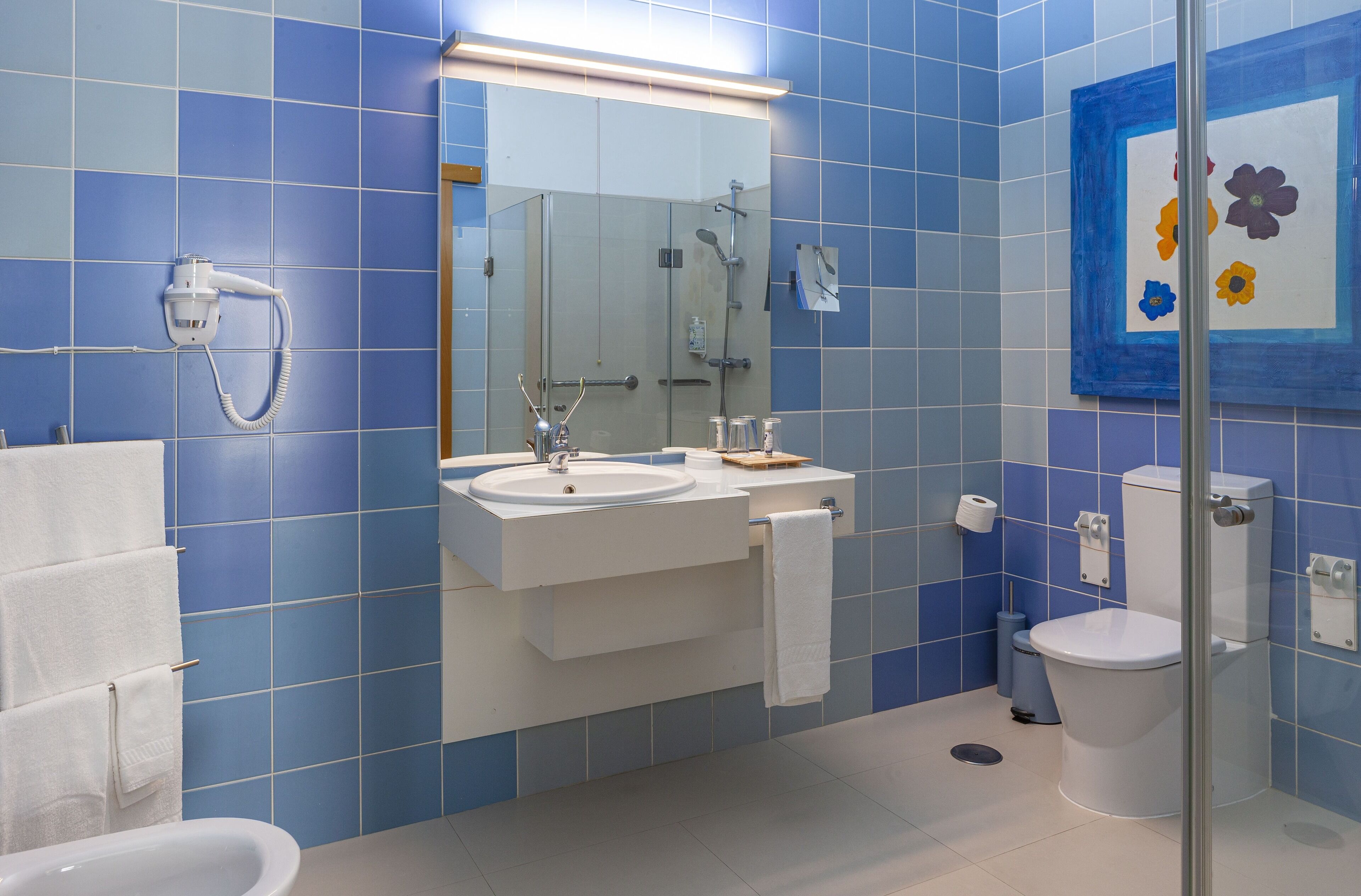 Une salle de bain avec des carreaux bleus, un lavabo blanc, un miroir, des toilettes et une douche.