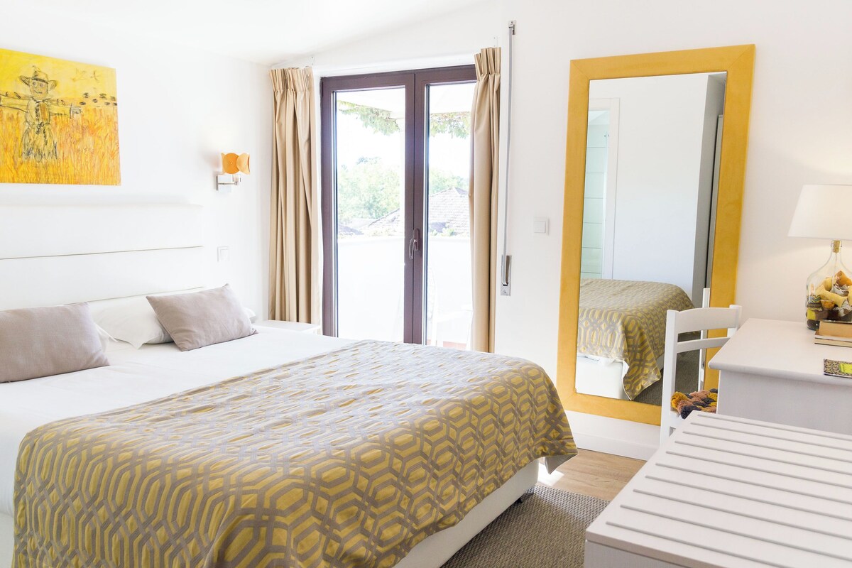 Una habitación de hotel con cama, escritorio, silla, ventana con cortinas y puerta.