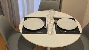 A round dining table with two white plates, two clear glasses, and a fork and spoon set. The table is surrounded by four grey chairs.