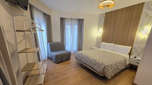 A modern hotel room with a large bed, a chair, a wardrobe, and a TV mounted on the wall.