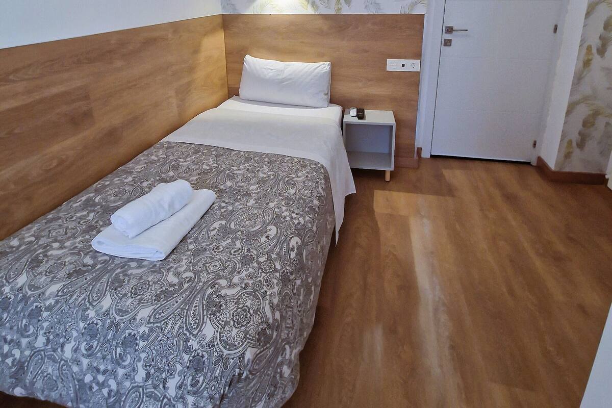 A hotel room with a bed, a nightstand, a wall-mounted lamp, and a door.