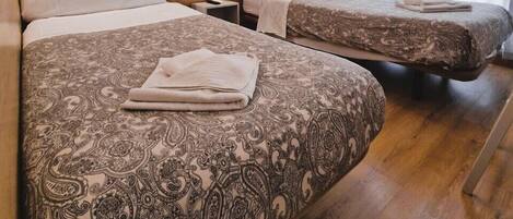 A hotel room with two beds, wooden headboards, patterned bedspreads, and a wall with a wheat leaf wallpaper.