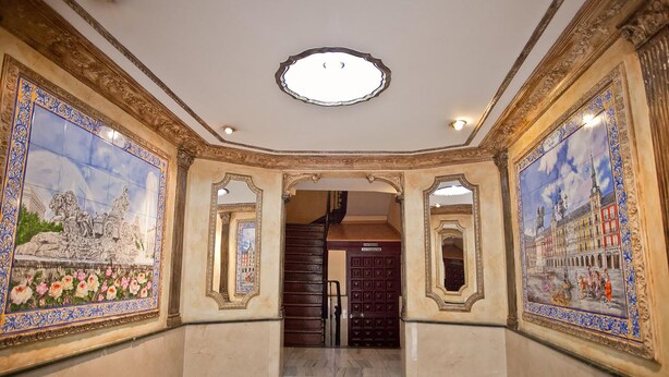 A grand hallway with ornate tile murals, a marble floor, and a staircase leading to an upper level.