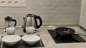 A kitchen with white tiled backsplash, a coffee maker, a kettle, and a frying pan on an induction cooktop.