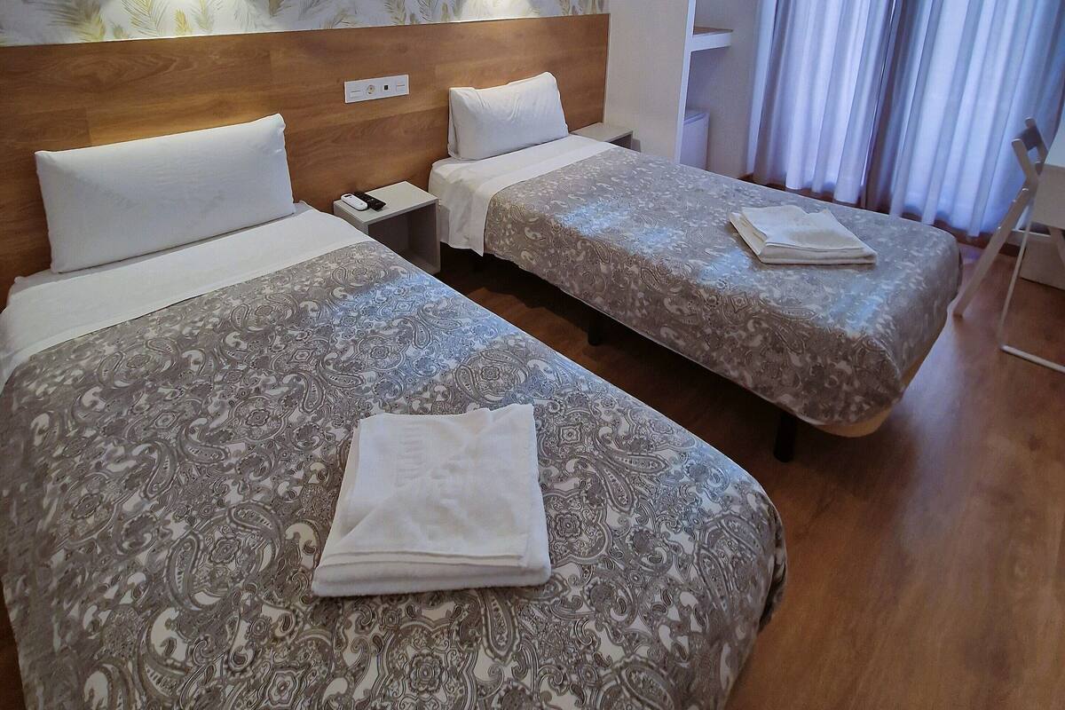 A hotel room with two beds, a wooden headboard, a nightstand, a white cabinet, and a potted plant.