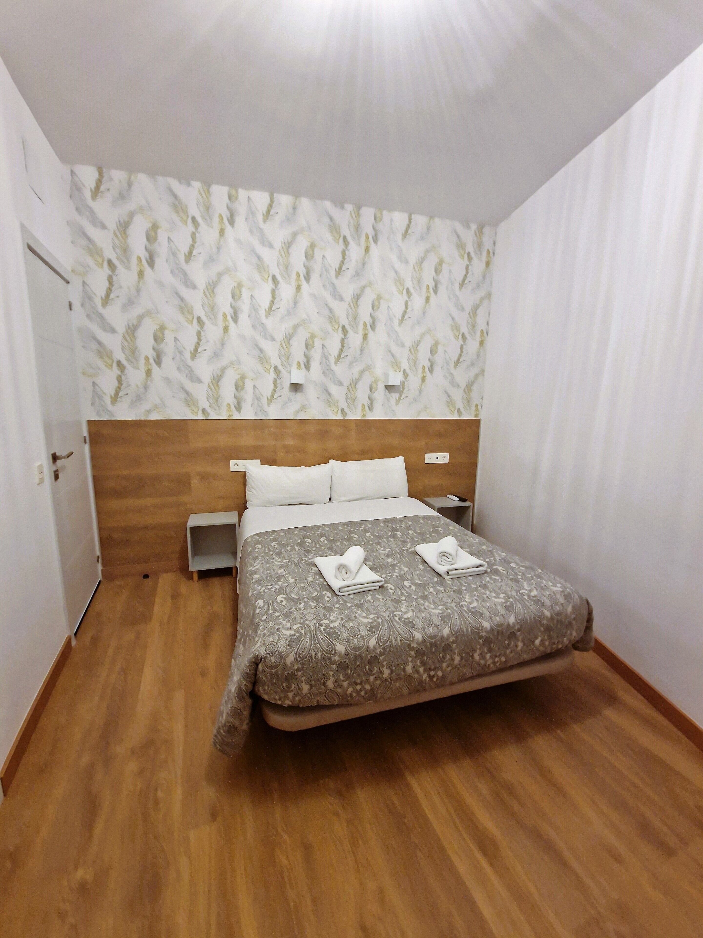 A bedroom with a wooden headboard, a patterned bedspread, and a nightstand with a lamp.