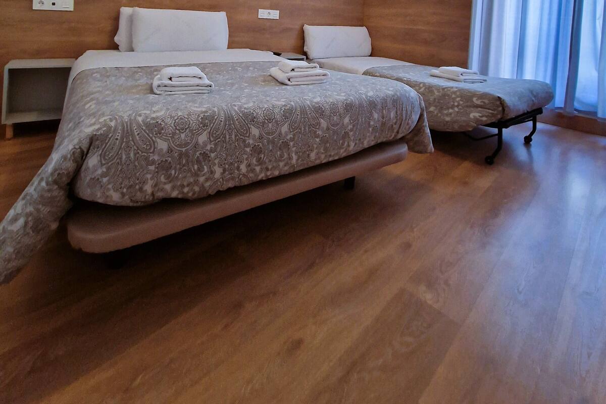 A hotel room with two beds, a wooden headboard, a patterned wall, and a large window with curtains.
