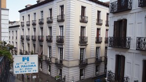 A multi-story building with balconies, a sign indicating it is a hotel, and a street with parked cars.