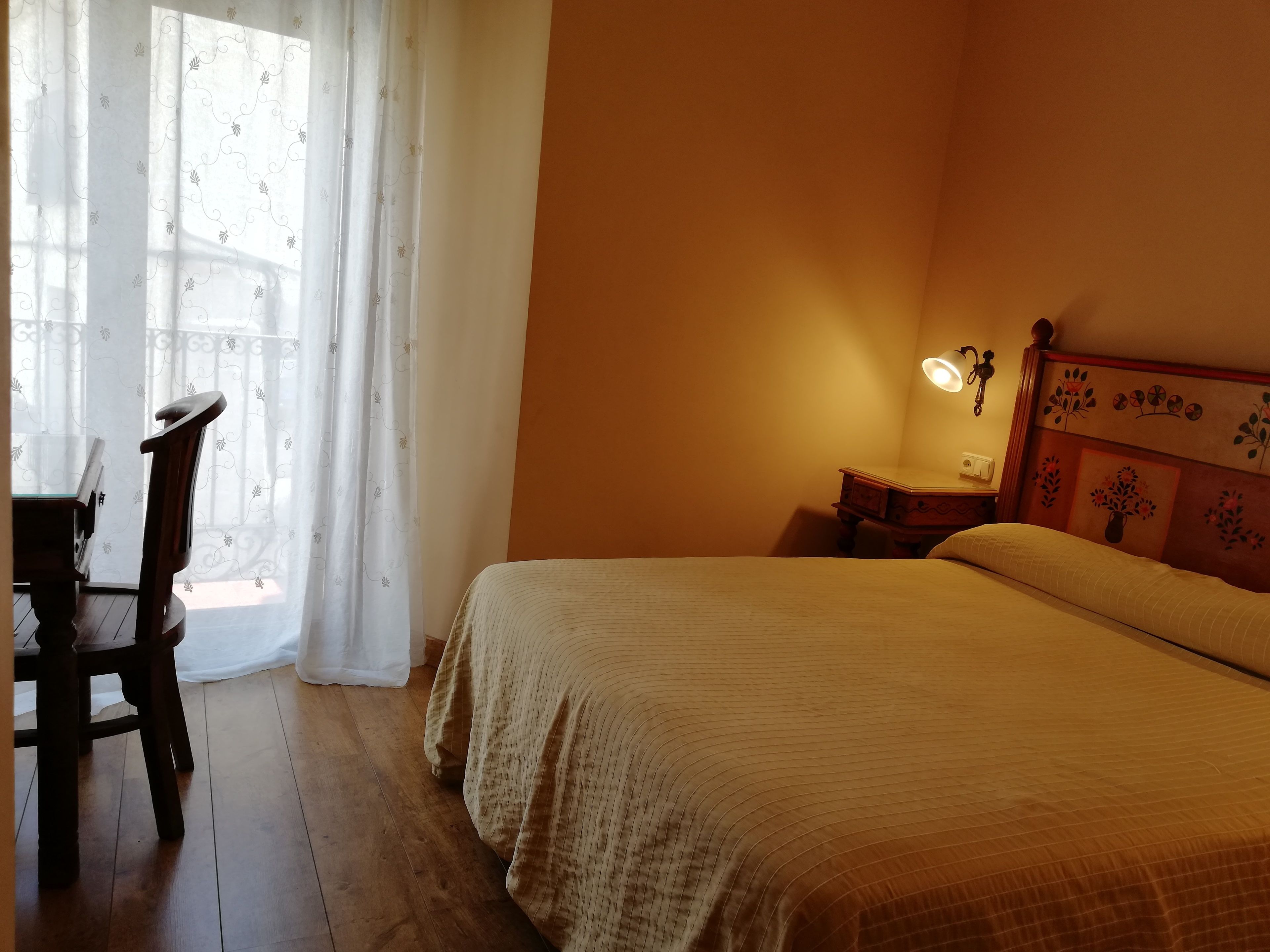 Ein Schlafzimmer mit Bett, Nachttisch, Lampe, Stuhl und einem Fenster mit Vorhängen.