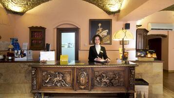 A reception desk with a person seated behind it, a framed artwork on the wall, and a lamp on the right.