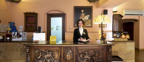 A reception desk with a person seated behind it, a framed artwork on the wall, and a lamp on the right.