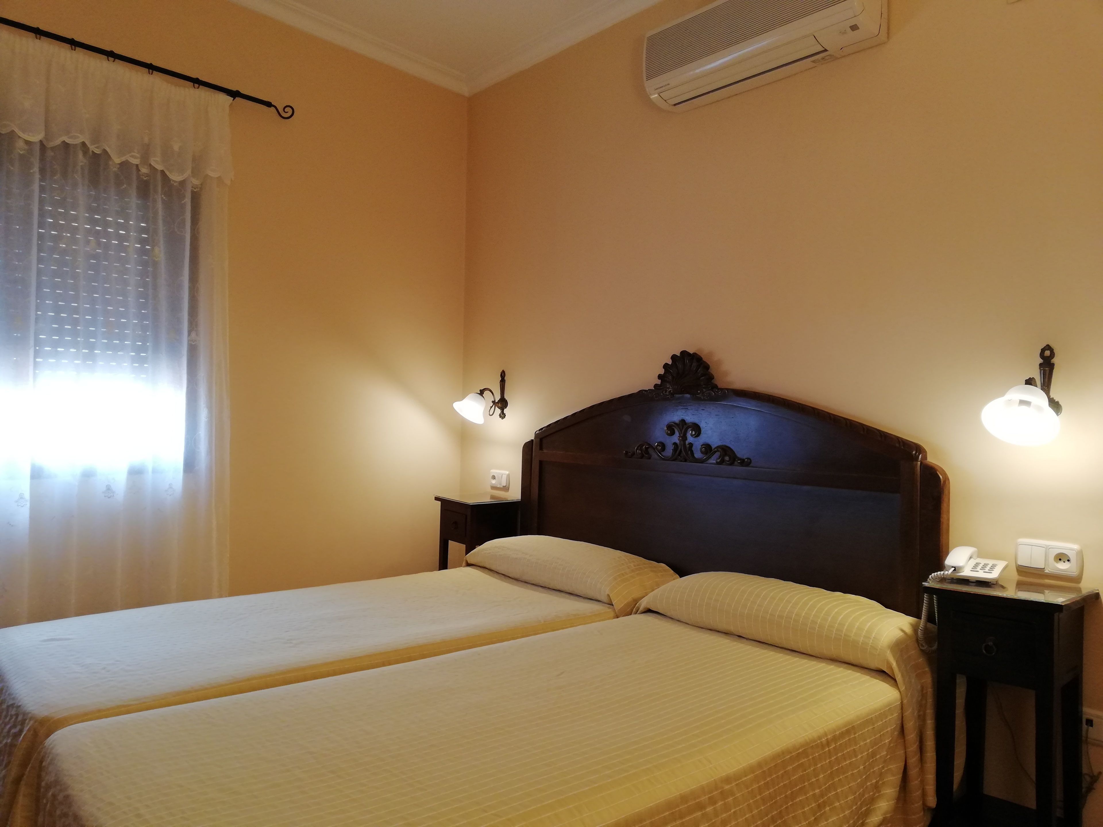 Une chambre d’hôtel avec deux lits, une table de chevet avec un téléphone, des lampes fixées au mur et un appareil de climatisation.