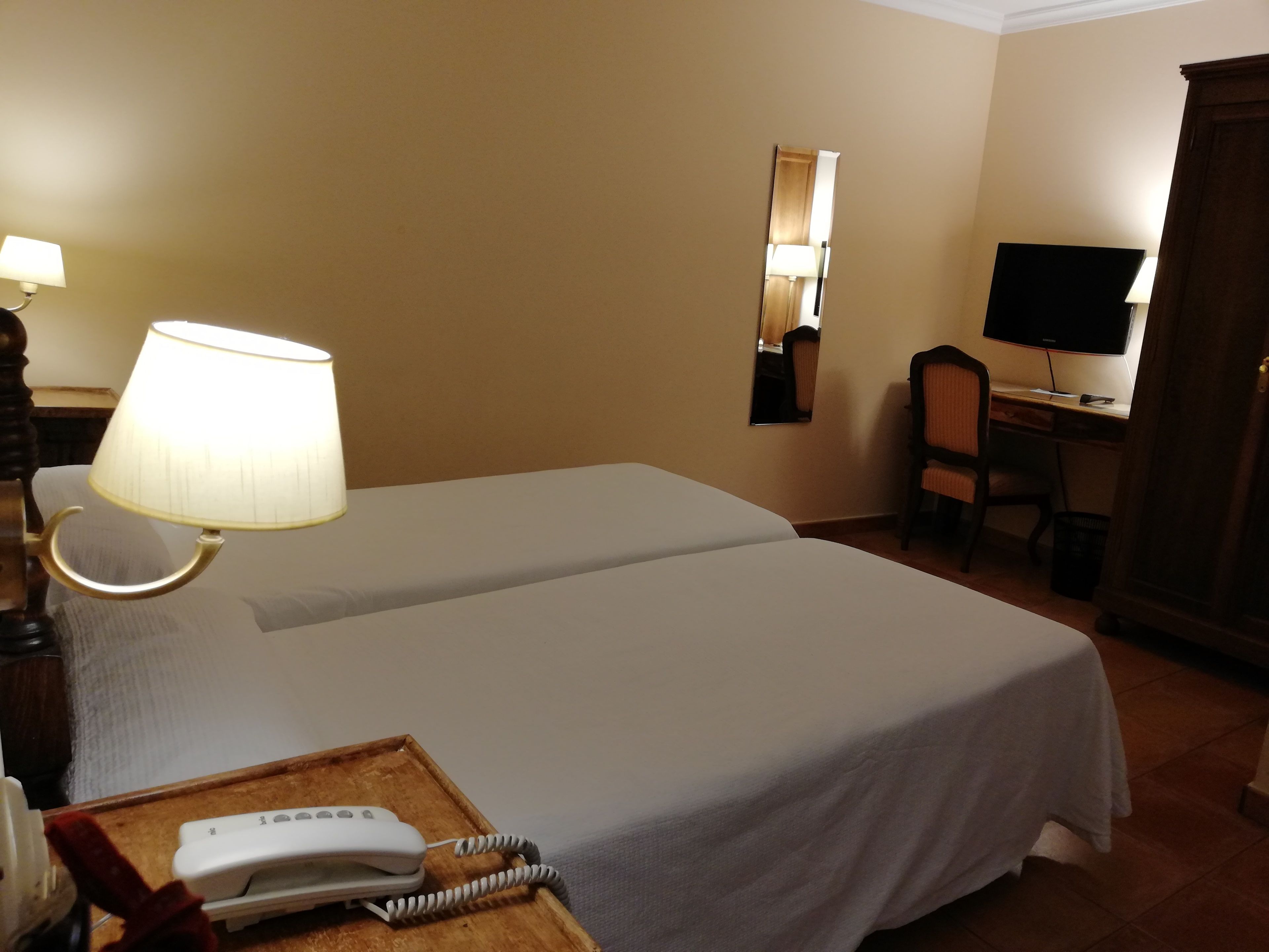 A hotel room with two beds, a desk with a computer, a telephone, and a lamp.