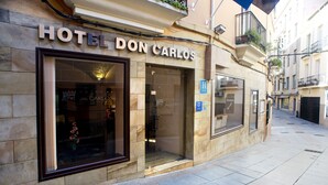 Exterior del Hotel Don Carlos, con una entrada amplia, una recepción visible y una vista despejada de la calle.