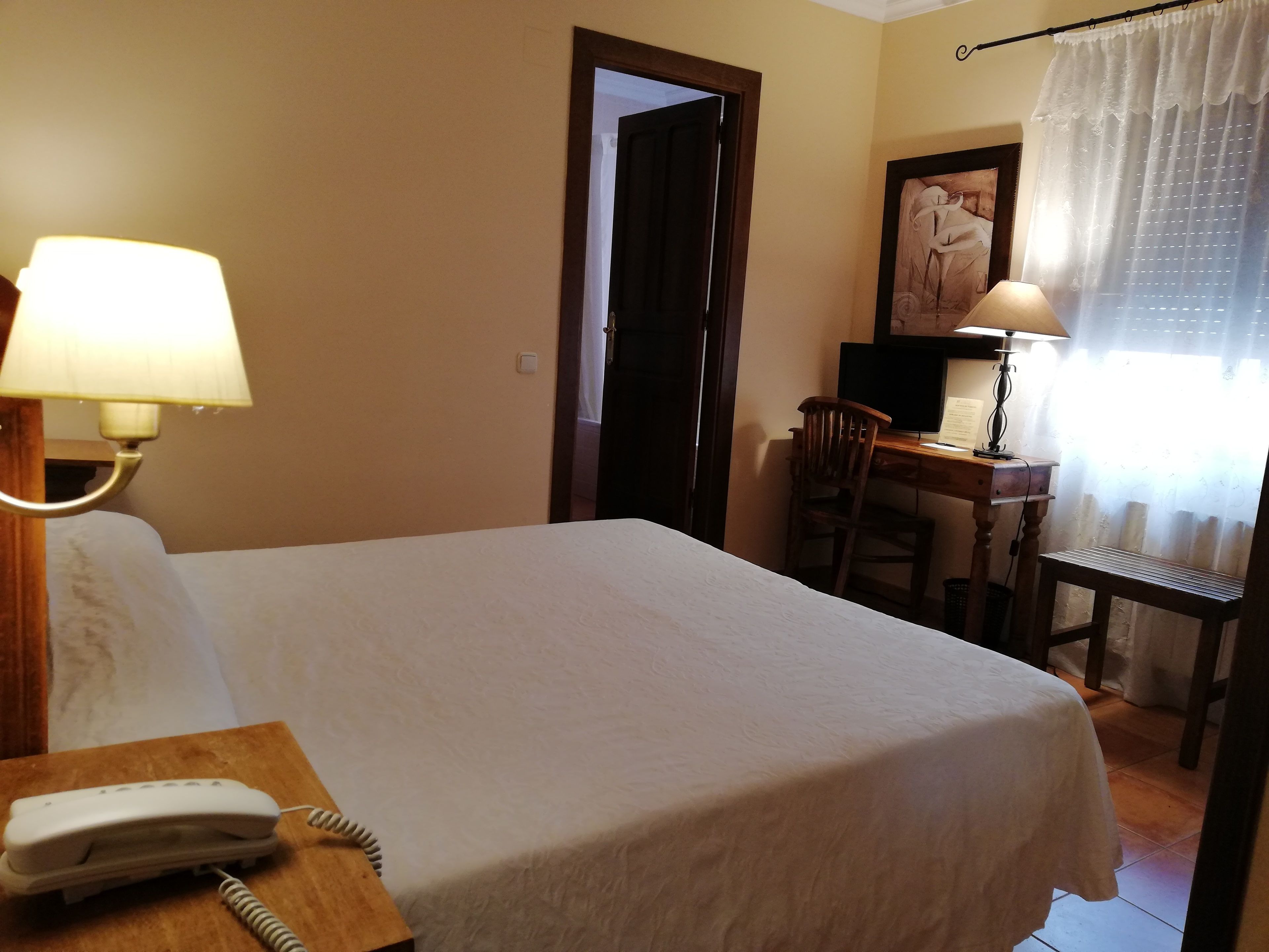 Ein Hotelzimmer mit einem Bett, einem Schreibtisch mit Computer, einem Stuhl, einer Lampe und einem Telefon.