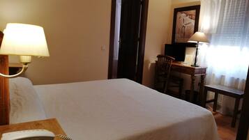 Ein Hotelzimmer mit einem Bett, einem Schreibtisch mit Computer, einem Stuhl, einer Lampe und einem Telefon.