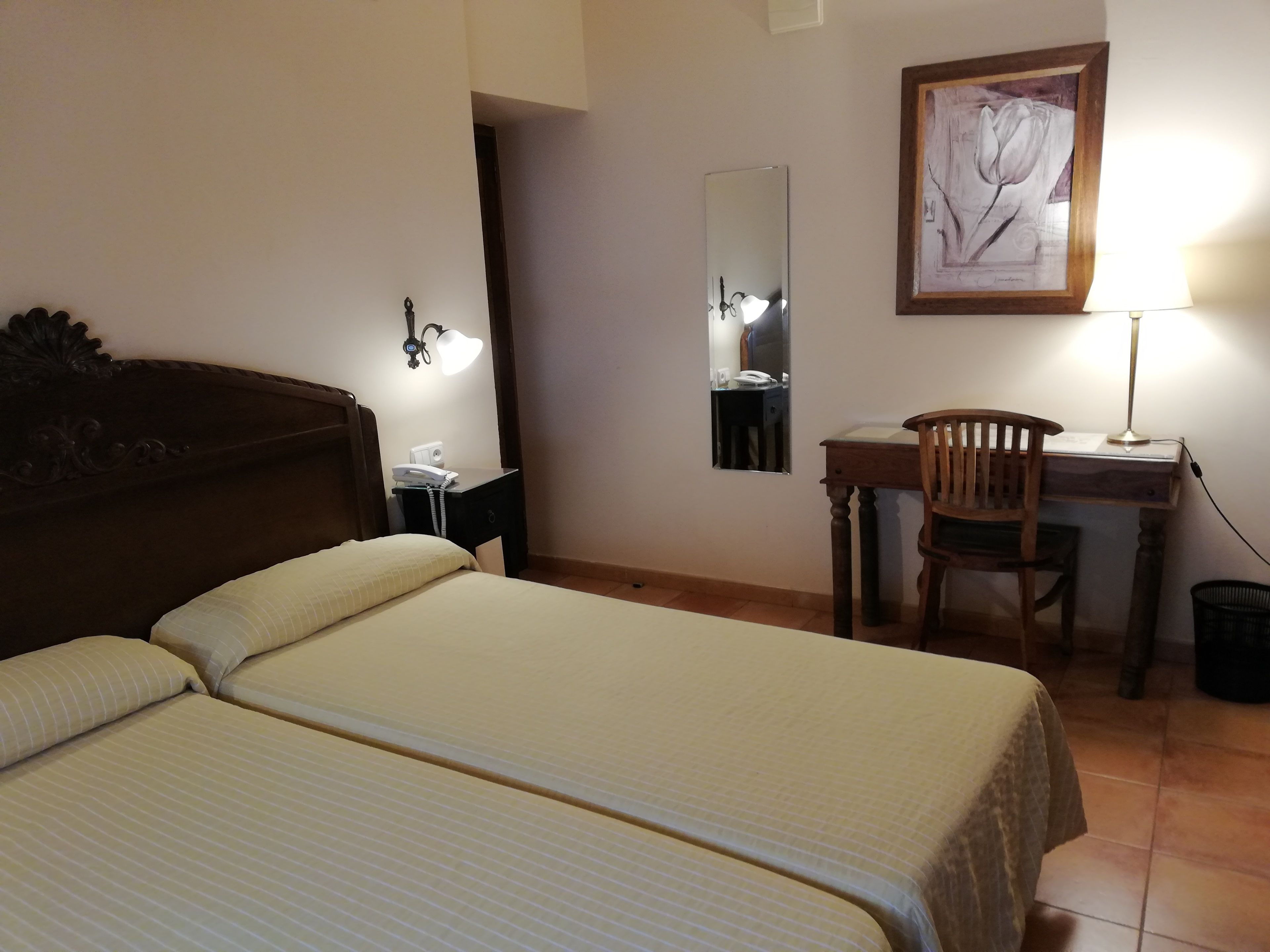 Habitación de hotel con dos camas, un escritorio, una silla, una lámpara, un teléfono y un cuadro en la pared.