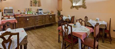 Un comedor con mesas y sillas de madera, una barra de buffet con comida y bebidas, y un espejo en la pared.