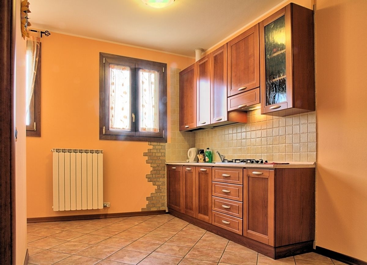 Cozinha com armários de madeira, painel de azulejos, janela com cortinas e radiador.
