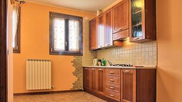 Cozinha com armários de madeira, painel de azulejos, janela com cortinas e radiador.