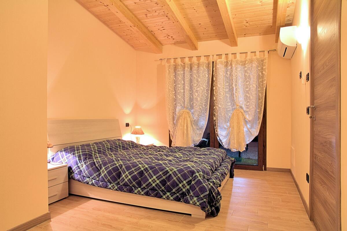 Une chambre à coucher avec un lit, une table de chevet, une lampe, un plafond en bois et une porte.