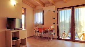 Una habitación con una televisión sobre un mueble de madera, una mesa de comedor con sillas, un ventanal corredizo con cortinas y un equipo de aire acondicionado en la pared.