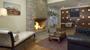 A cozy living room with a stone fireplace, comfortable seating, a flat-screen TV, and a bookshelf.