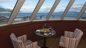 A dining area with a table set for two, a view of the sea, and a ship in the distance.