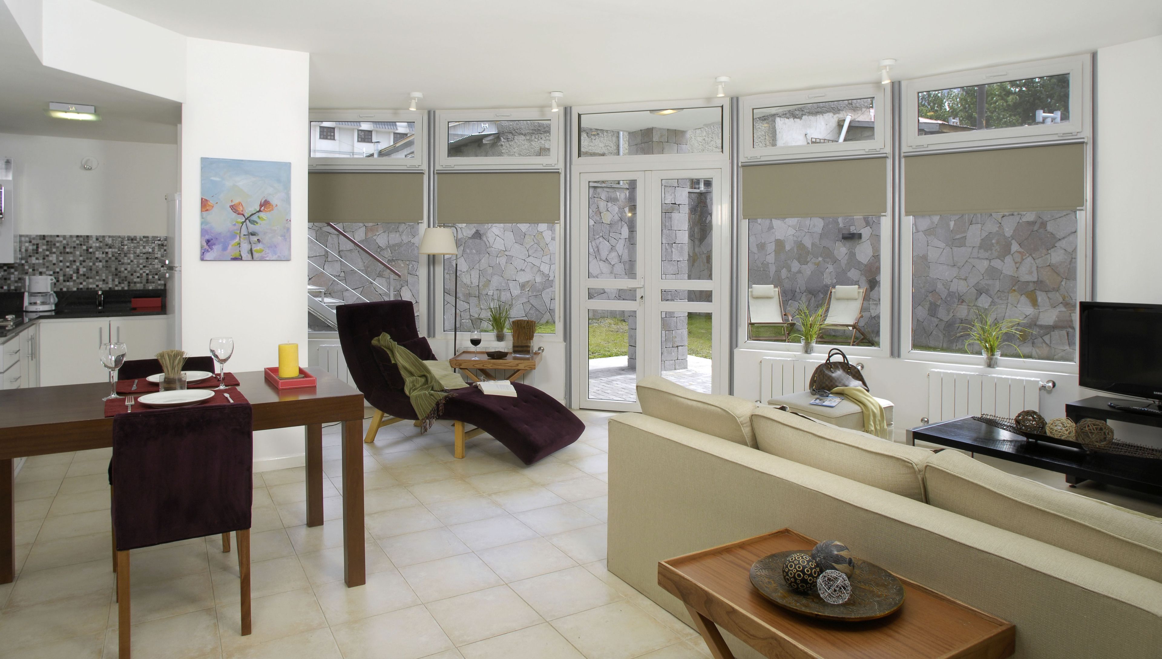 A modern living room with a dining area, large windows, and a stone wall.