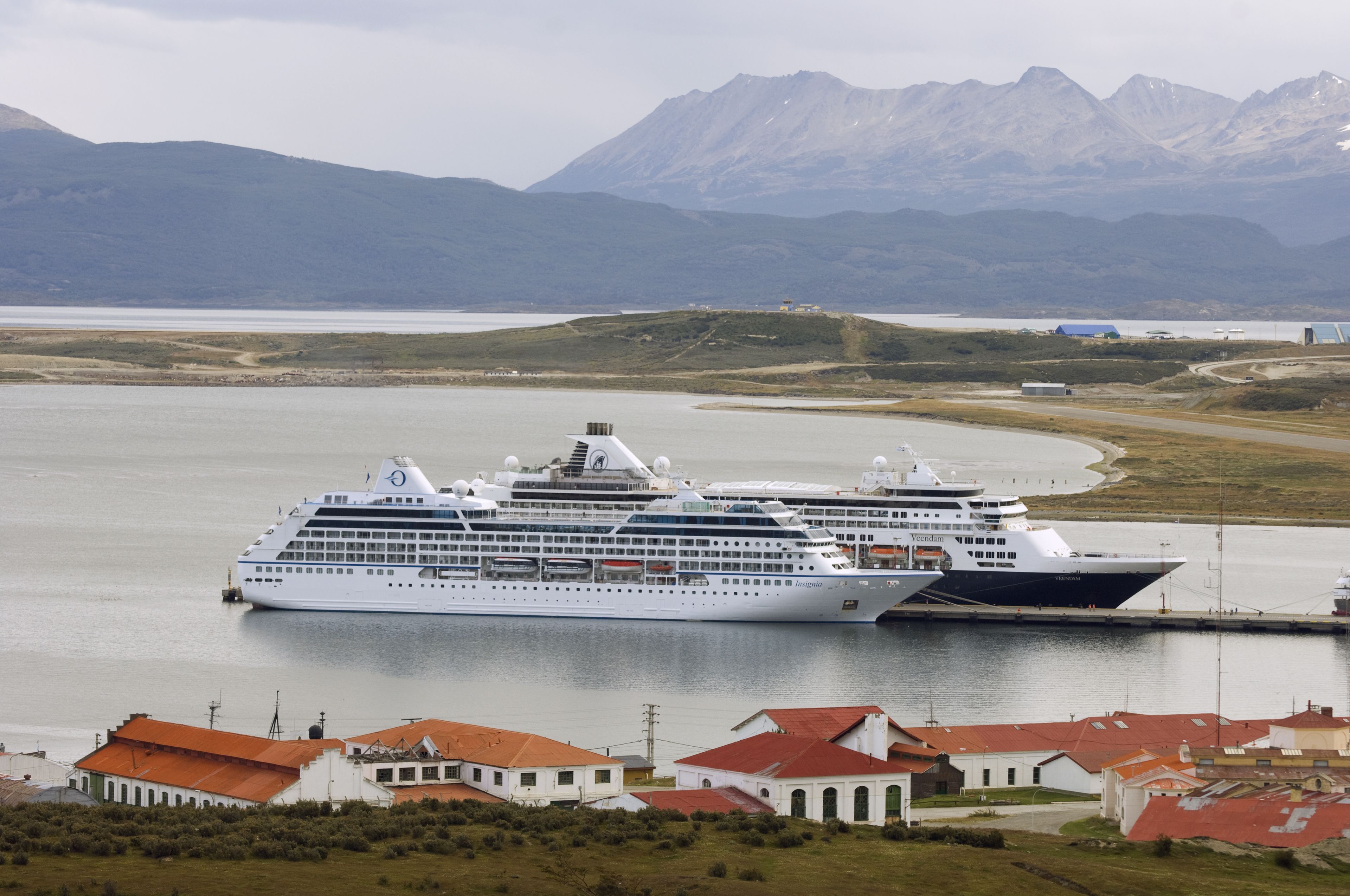 A large cruise ship docked at a port with a mountainous backdrop.