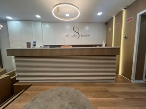 A hotel reception desk with a modern design, a reception area, and a sign indicating the hotel name. - Hotel Seculo (Porto)