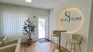A hotel reception area with a modern design, featuring a reception desk, seating area, and a potted plant. - Hotel Seculo (Porto)