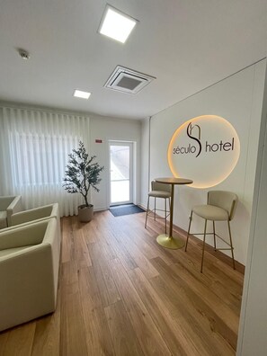 A hotel reception area with a modern design, featuring a reception desk, seating area, and a potted plant. - Hotel Seculo (Porto)