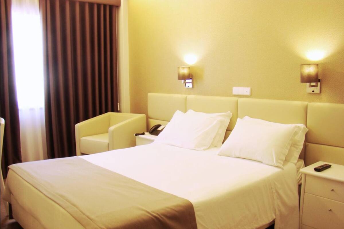 Ein Hotelzimmer mit einem großen Bett, zwei Nachttischen, einem Sessel und zwei Wandleuchten.