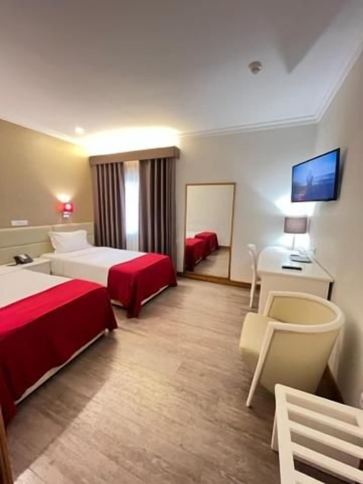 Habitación de hotel con dos camas, un escritorio, una silla, un televisor y un espejo.