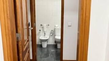 A narrow hallway leading to a bathroom with two toilets and a sink.