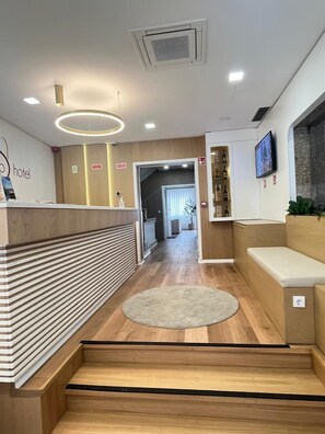 A hotel reception area with a reception desk, a seating area, a television, and a hallway leading to other rooms. - Hotel Seculo (Porto)