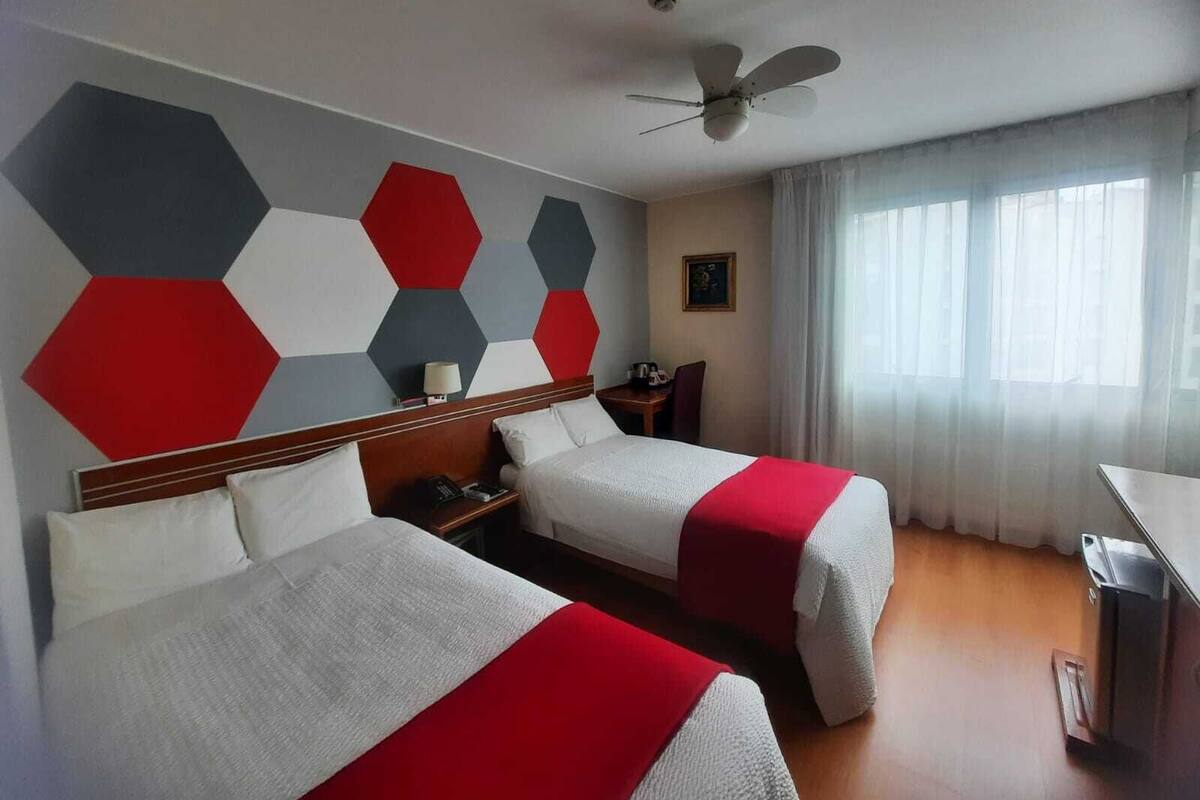 A hotel room with two beds, a ceiling fan, a desk, and a window with curtains.