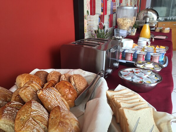 A breakfast buffet with various breads, pastries, and yogurt containers.