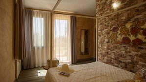 Un dormitorio con una cama grande, un sillón estampado, una pared de piedra con un mural floral y un suelo de madera.