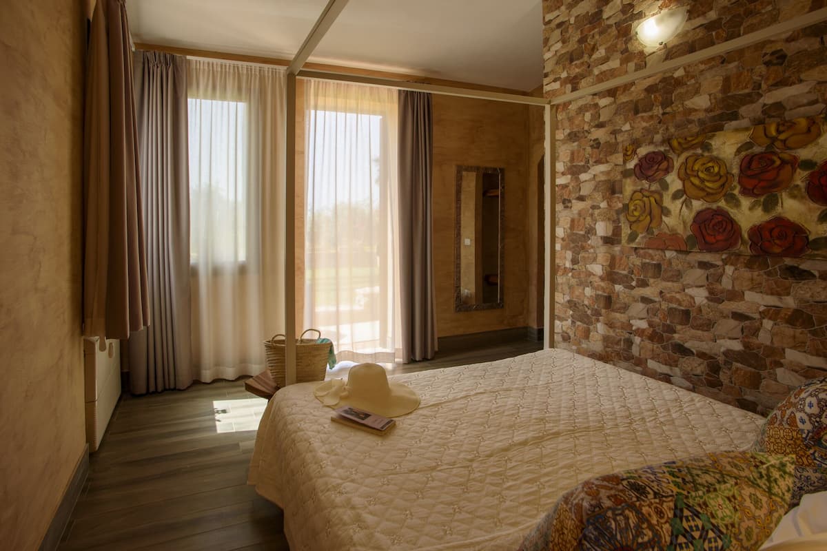 Une chambre avec un grand lit, un fauteuil à motifs, un mur en pierre orné d’une fresque florale et un plancher en bois.