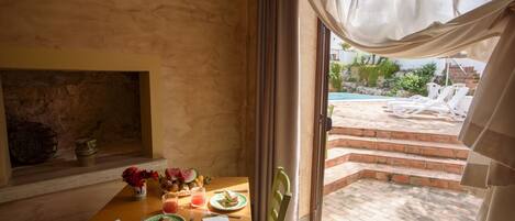 Zona pranzo con tavolo apparecchiato per due, un vaso di fiori e vista su piscina e area relax all'aperto.