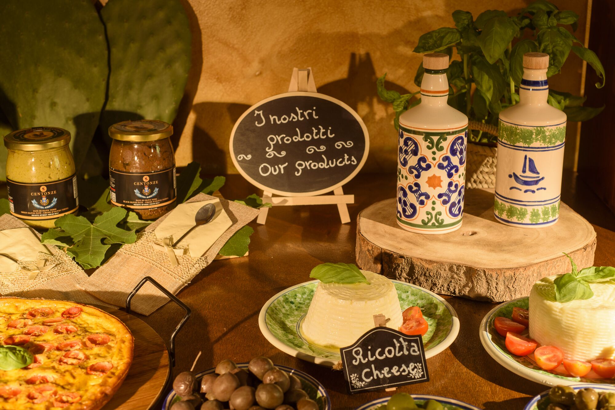 Exhibición de alimentos con varios quesos, una pizza y un cartel que indica 'Ricotta Cheese'.
