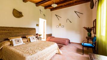 Un dormitorio con una cama grande, un cabecero de madera, una silla, una mesita y una puerta.
