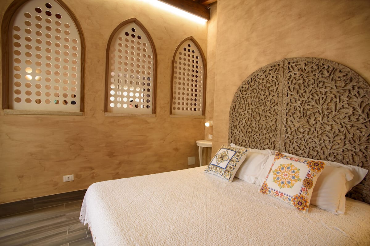 Une chambre à coucher avec un grand lit, trois fenêtres en arc de cercle et une tête de lit décorative.